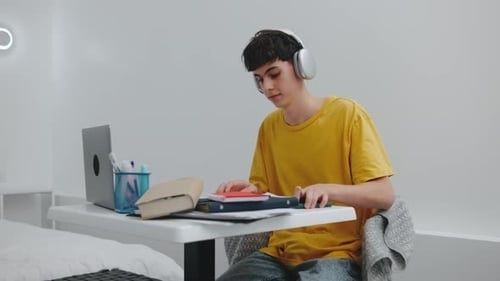 Ung person med hörlurar studerar vid ett skrivbord med en laptop
