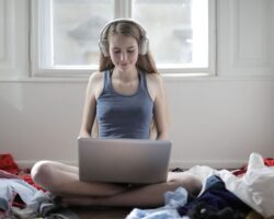 Person med hörlurar använder laptop medan hen sitter bland kläder
