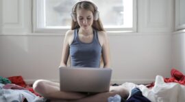 Person med hörlurar använder laptop medan hen sitter bland kläder