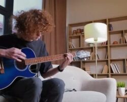 Vuxen person spelar akustisk gitarr i ett vardagsrum