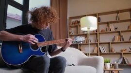 Vuxen person spelar akustisk gitarr i ett vardagsrum
